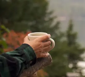 Man holding coffee while looking out at lake